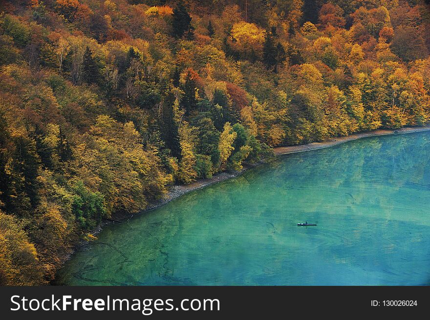 Unrecognizable Fisherman In A Boat On A Lake And Autumnal Forest On A Bank. Photo With Very Highlighted Colors.