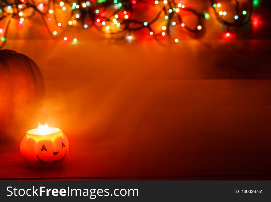 Halloween candle in the dark on a wooden background. Behind the pumpkin in the lights of the garland