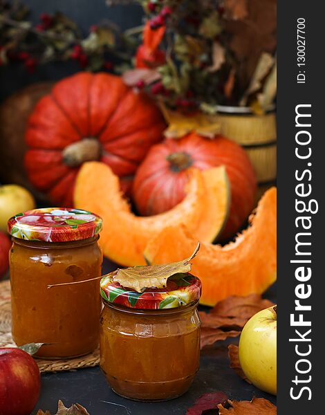 Puree pumpkin and apple for children, located in banks against a dark background. On the table are apples and pumpkins. Autumn still life