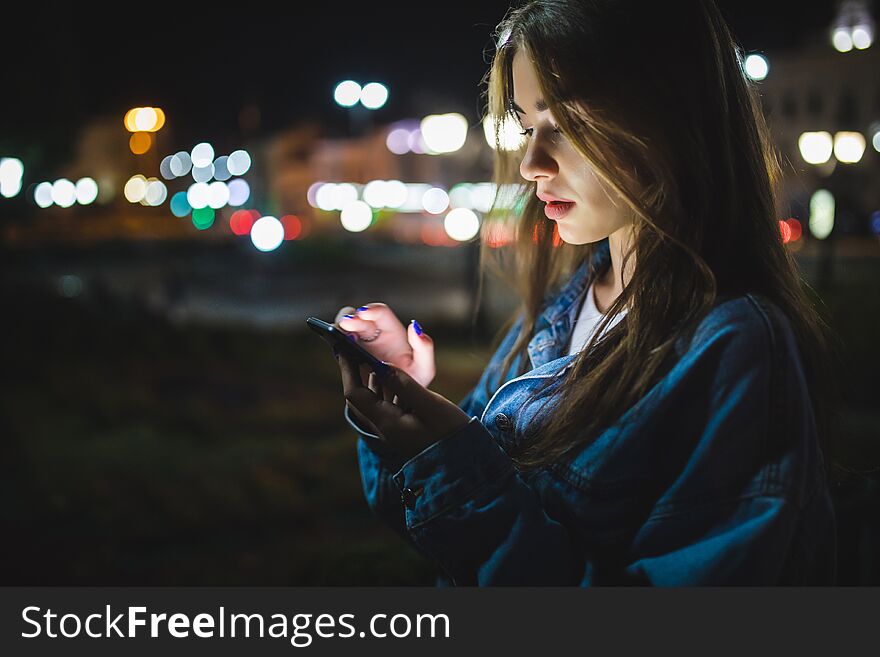 Woman using smart phone mobile in the city at night on light bokeh