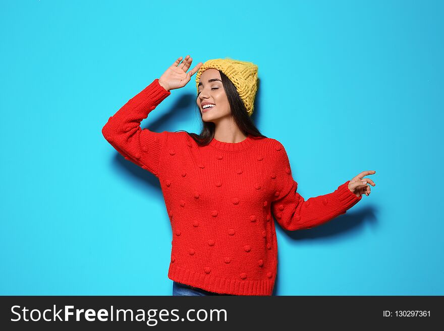 Young woman in warm sweater and hat on color background