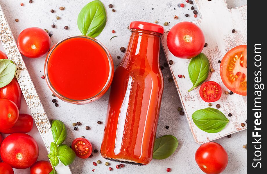 Bottle of fresh organic tomato juice with fresh raw tomatoes basil and pepper in box on stone kitchen background