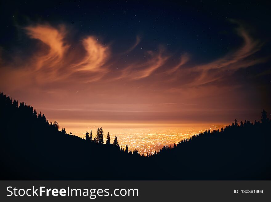 Glowing City lights at night sky with stars and silhouettes of pine tree and mountain in Almaty, Kazakhstan. Glowing City lights at night sky with stars and silhouettes of pine tree and mountain in Almaty, Kazakhstan.