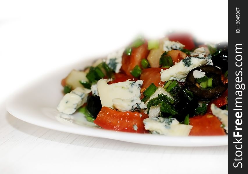 Salad with olives, tomatoes, green onion and blue cheese on a white plate