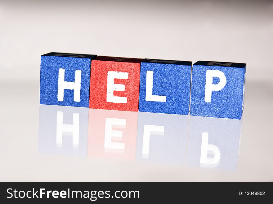 Closeup of colorful blocks spelling word help, reflected on white background.