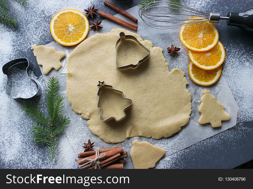 Christmas cookies. Cutting gingerbread. The process of baking cookies at home. Gingerbread dough for cookies, cookies, cinnamon sticks, orange and fir branches. New year or winter holidays still life, background. Top view. Christmas cookies. Cutting gingerbread. The process of baking cookies at home. Gingerbread dough for cookies, cookies, cinnamon sticks, orange and fir branches. New year or winter holidays still life, background. Top view