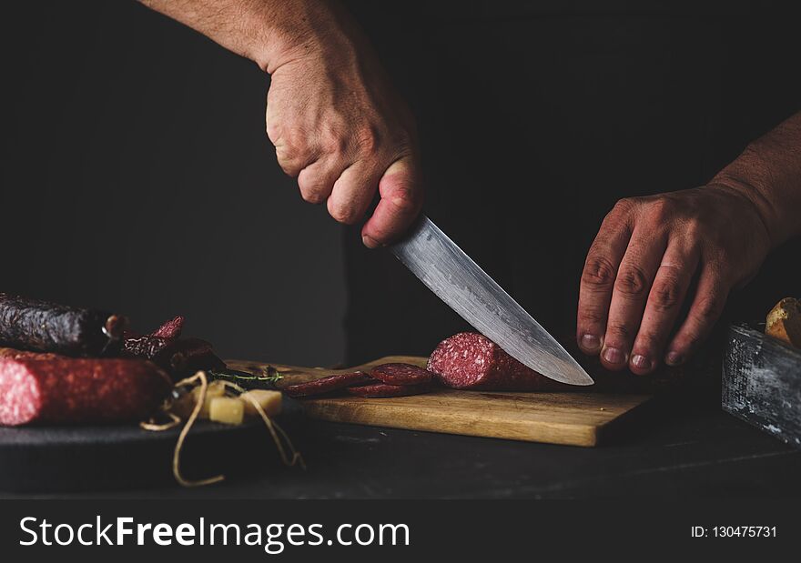 Men`s hands cut sausage salami on a cutting board.