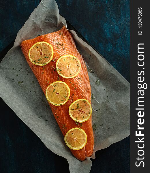 Raw fillet of salmon with lemons on a baking sheet.