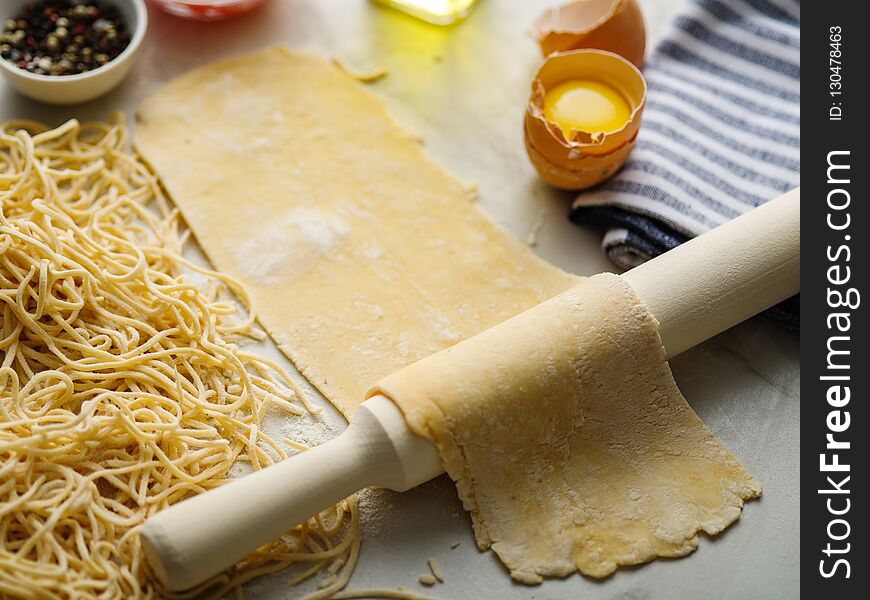 Homemade pasta dough is being processed. Rolled dough for homemade italian uncooked pasta over white marble texture background. Homemade pasta dough is being processed. Rolled dough for homemade italian uncooked pasta over white marble texture background.