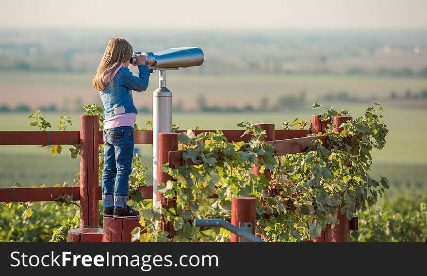 Little blond girl standing on the sp in the wooden fance of the Moravian field and looking into spyglass. Little blond girl standing on the sp in the wooden fance of the Moravian field and looking into spyglass