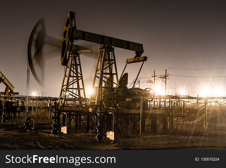 Working oil pump jack at night time. Oilfield during winter. Refinery lights background. Oil and gas concept. Toned.