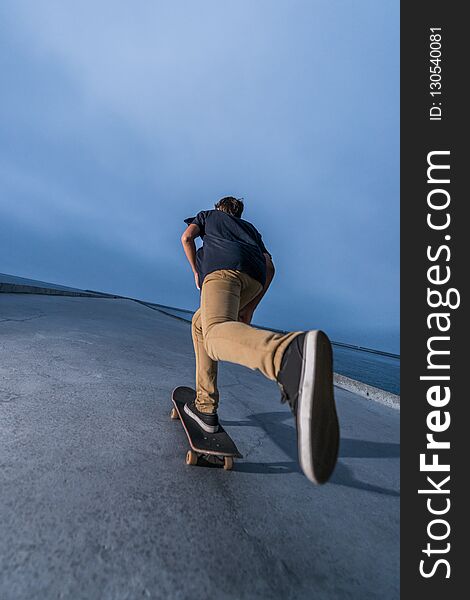 Skateboarder pushing on a concrete pavement along the harbour during the sunset.