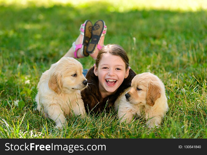 Girl is on a stroll with golden retriever puppies. Child is laying on grass between two wonderful furry balls. Lovely outdoor photo. Girl is on a stroll with golden retriever puppies. Child is laying on grass between two wonderful furry balls. Lovely outdoor photo.
