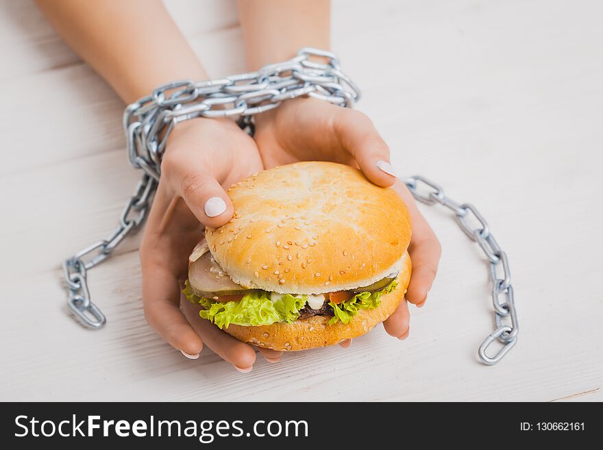 Steel chain-bound female hands with burger. Concept weight loss, junk food