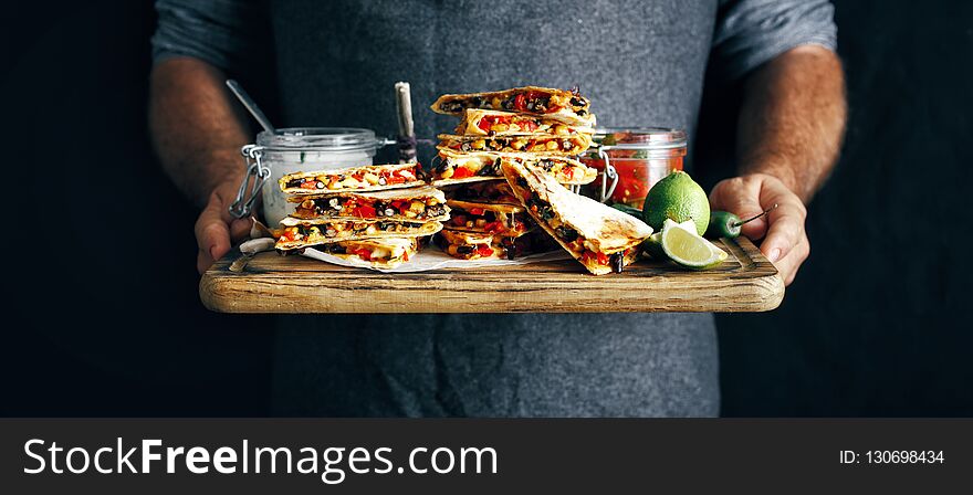 In the hands man cutting board with vegetarian snacks: quesadilla with vegetables and cheese on dark background. In the hands man cutting board with vegetarian snacks: quesadilla with vegetables and cheese on dark background