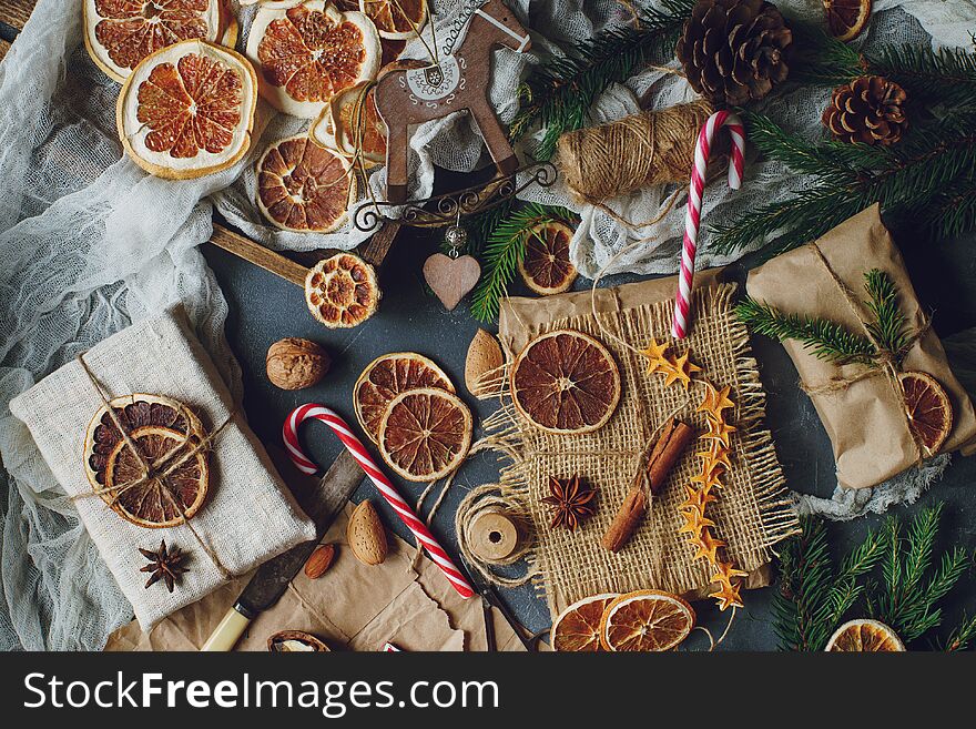 Christmas or New Year composition with handmade gifts, dry oranges, cinnamon, fir tree on dark stone table. Holidays preparations