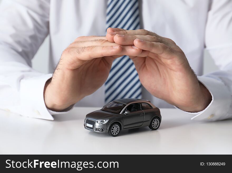 Male insurance agent covering toy car at table, closeup