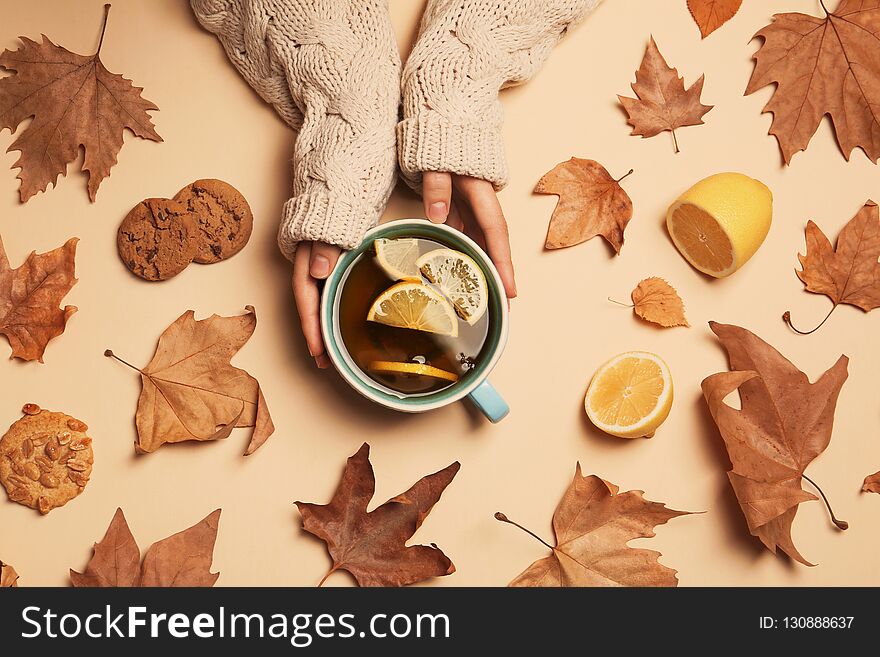 Woman in autumn sweater holding cup of hot cozy drink on color background, top view