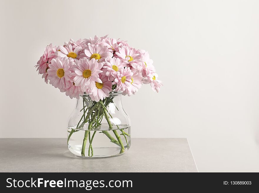 Vase with beautiful chamomile flowers on table against light background. Space for text