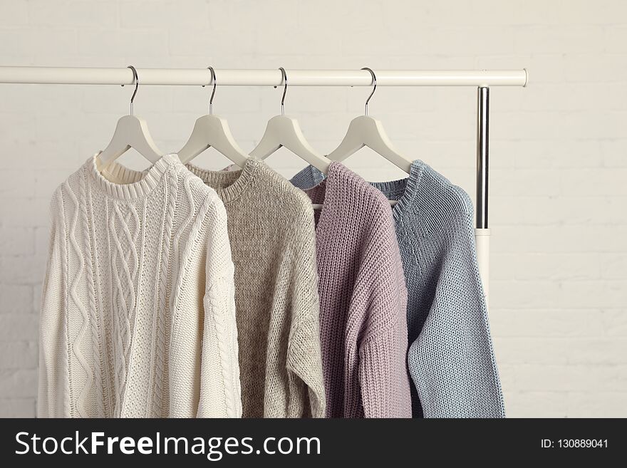 Collection of warm sweaters hanging on rack against white brick wall