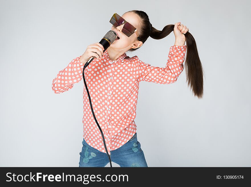 Girl in orange shirt, glasses and blue jeans on grey background. Girl in orange shirt, glasses and blue jeans on grey background.