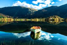 Autumn Landscape With A Lone Boat, Mountains, Colorful Trees And Blue Sky Reflected In Lake Stock Photos Autumn Landscape With A Lone Boat, Mountains, Colorful Trees And Blue Sky Reflected In Lake Stock Photos