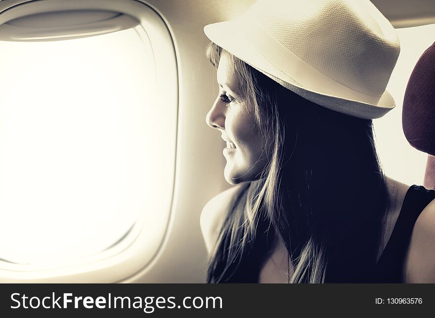 Young woman is looking through a window in the atplane. Pastel colors. Great vacation and travel concept. Young woman is looking through a window in the atplane. Pastel colors. Great vacation and travel concept