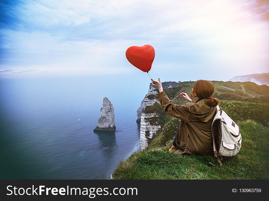 Happy girl with a red balloon in the shape of a heart at background of scenery Etretat. France. Happy girl with a red balloon in the shape of a heart at background of scenery Etretat. France