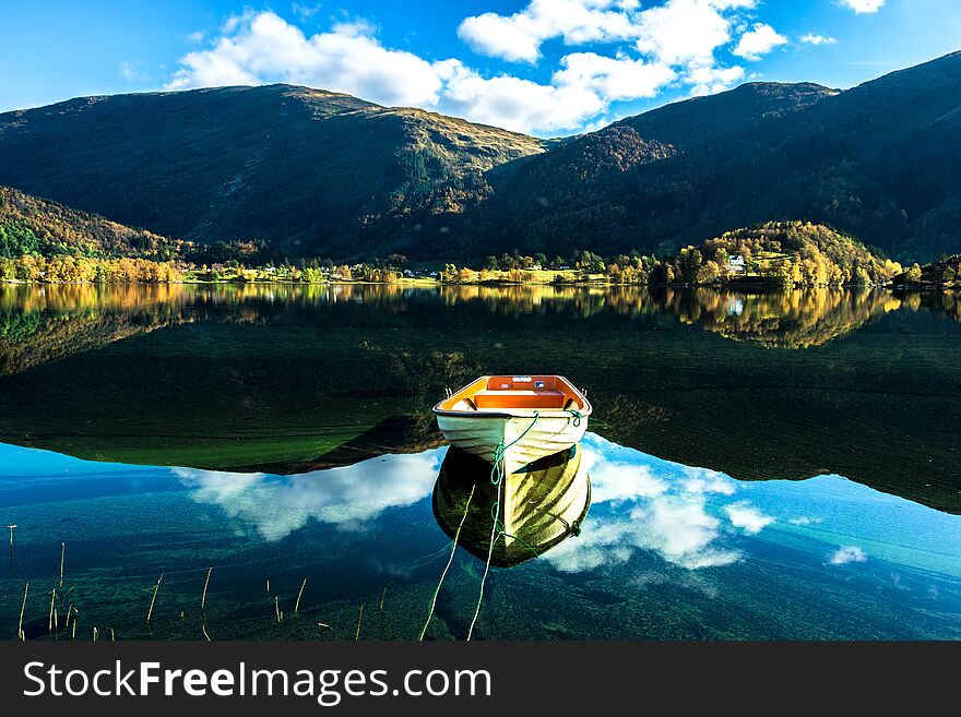 Autumn Landscape with A Lone Boat, Mountains, Colorful Trees and Blue Sky Reflected in Lake