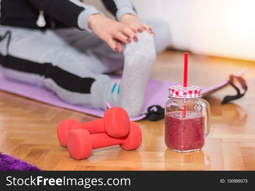 Dumbbell and smoothie in retro jar on floor and woman working stretching exercises legs