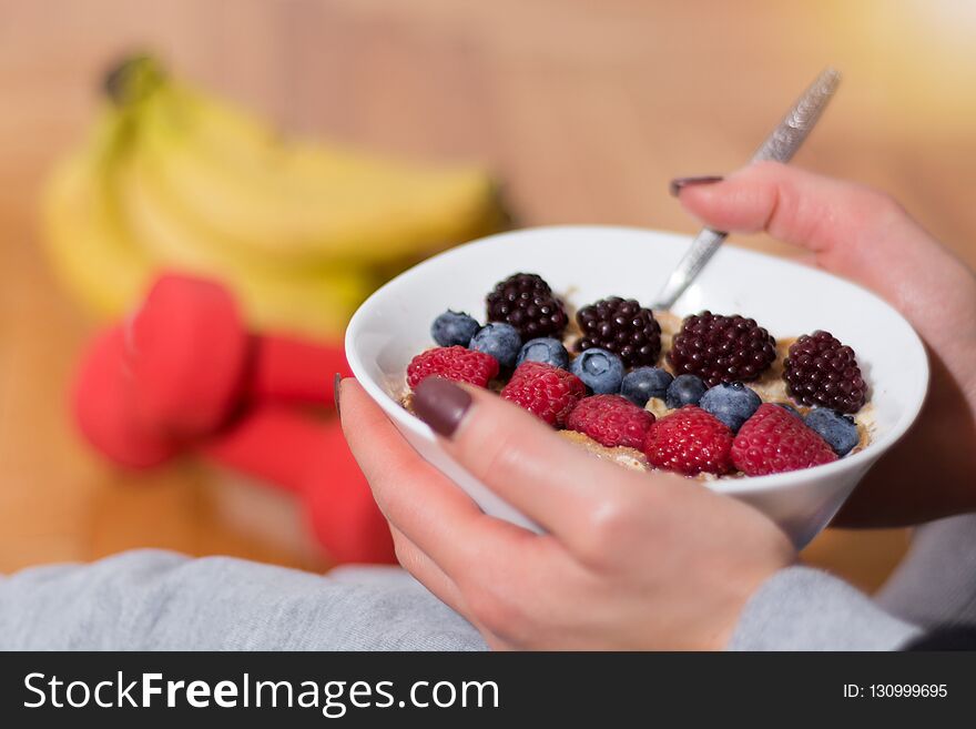 Woman eating Oats porridge in bowl decorated with blackberries, raspberries and blueberries