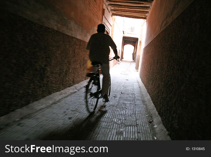 A man rides his bicycle on an empty narrow street. A man rides his bicycle on an empty narrow street