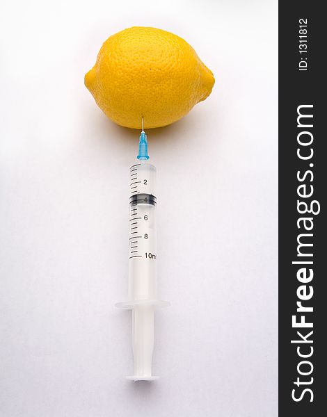 A bright yellow lemon being injected with a clear syringe. Illustrating food safety issues, Genetic engineering, and health. A bright yellow lemon being injected with a clear syringe. Illustrating food safety issues, Genetic engineering, and health.