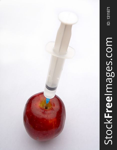 A bright red apple being injected with a clear syringe. Illustrating food safety issues, Genetic engineering, and health. A bright red apple being injected with a clear syringe. Illustrating food safety issues, Genetic engineering, and health.