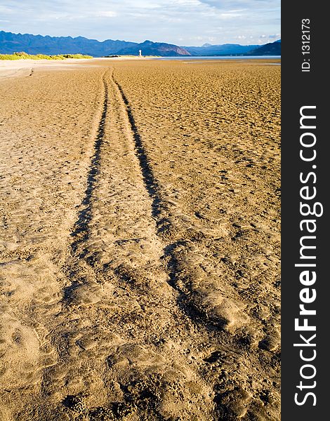 Vehicle tracks on a muddy and wet tidal marsh. There are mountains in a distance and a small lighthouse. Vehicle tracks on a muddy and wet tidal marsh. There are mountains in a distance and a small lighthouse.