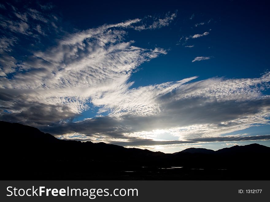Clouds backlit by a setting sun with a mountain range in the foreground. Clouds backlit by a setting sun with a mountain range in the foreground.