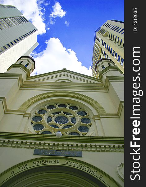 Picture of old Synagogue amid 2 towering converging buildings under a bright blue sky. Picture of old Synagogue amid 2 towering converging buildings under a bright blue sky