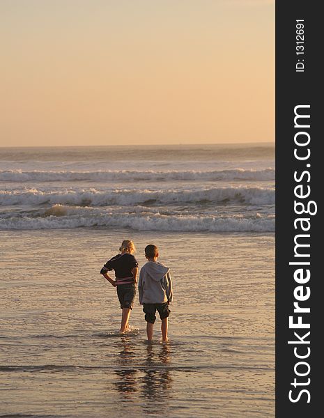 Two children waiting for the next wave to come in..lit by the late evening sun.  (#4 in a series of 4). Two children waiting for the next wave to come in..lit by the late evening sun.  (#4 in a series of 4).