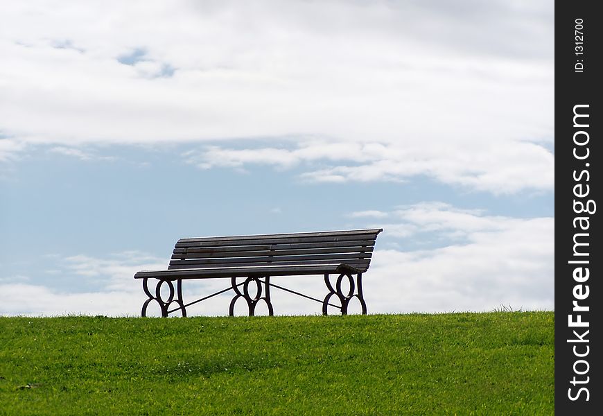Lone bench on grass with cloudy sky in the background. Lone bench on grass with cloudy sky in the background