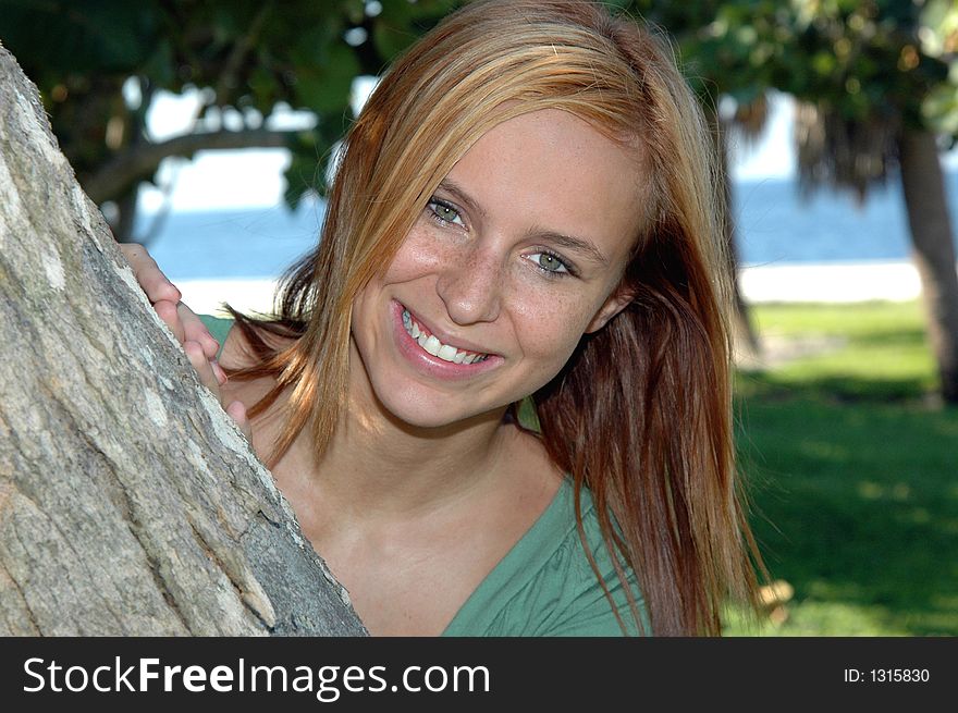 A pretty teenager peaking out from a  tree in the park. A pretty teenager peaking out from a  tree in the park