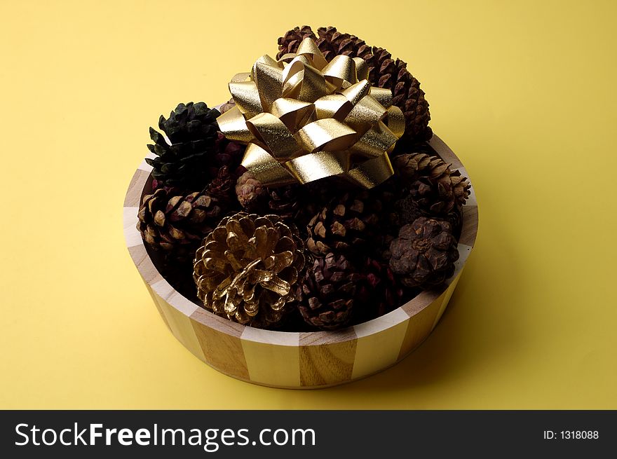 An arrangement of scented pinecones with a golden bow on yellow background. An arrangement of scented pinecones with a golden bow on yellow background