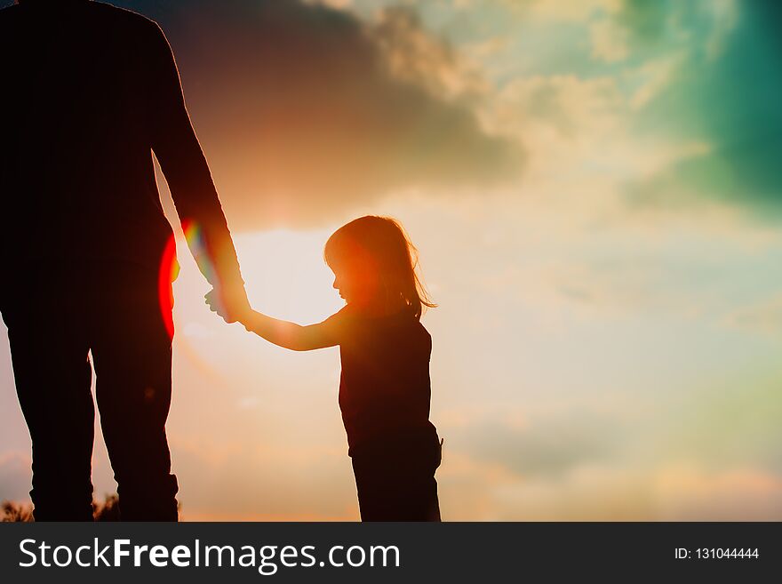 Silhouette of little girl holding parent hand at sunset sky