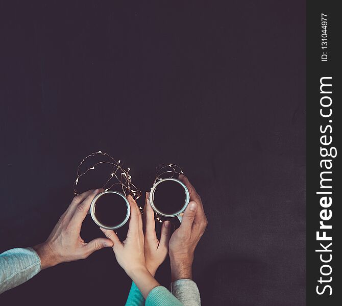 Couple in love holding hands with coffee on black table, with christmas lights. Photograph taken from above, top view