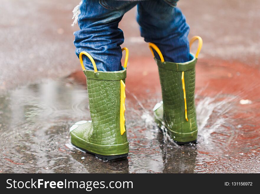 Child with rain boots jumps into a puddle