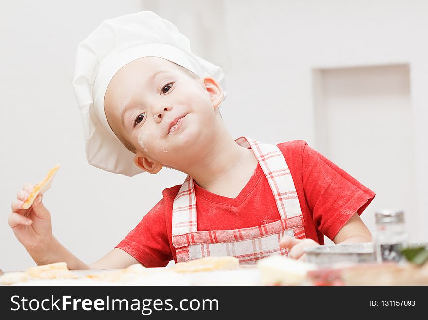 Little cheerful boy chef cooks and eats pizza