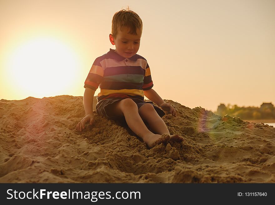 Four-year-old caucasian boy playing in the sand on the beach, summer sunset on the river bank in the sunlight sunbeam. Four-year-old caucasian boy playing in the sand on the beach, summer sunset on the river bank in the sunlight sunbeam