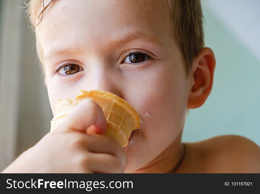 Small boy with charming eyes is holding and eating ice-cream dessert