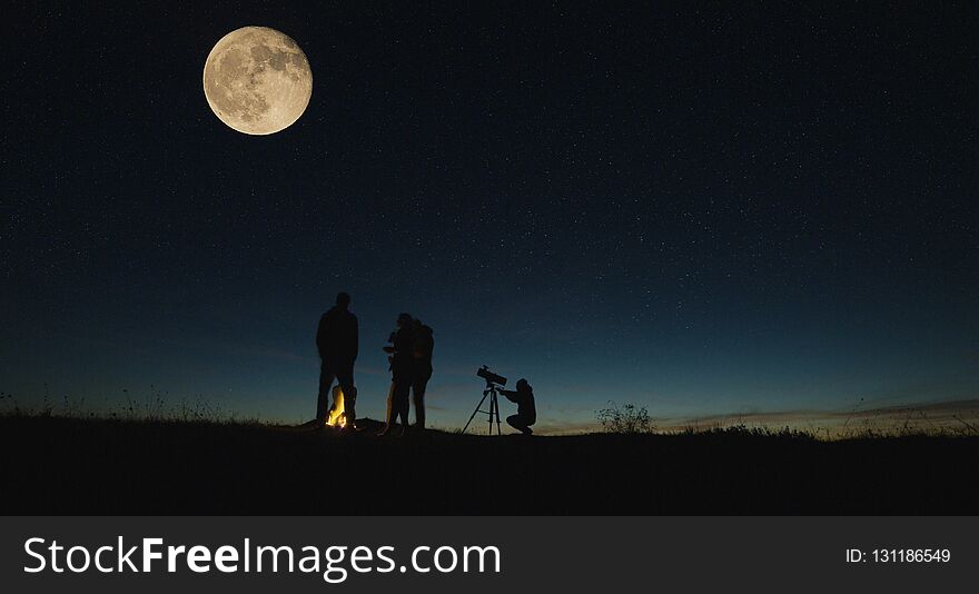 Silhouettes of people gathering together in nature looking on big moon with burning campfire near in night. Silhouettes of people gathering together in nature looking on big moon with burning campfire near in night