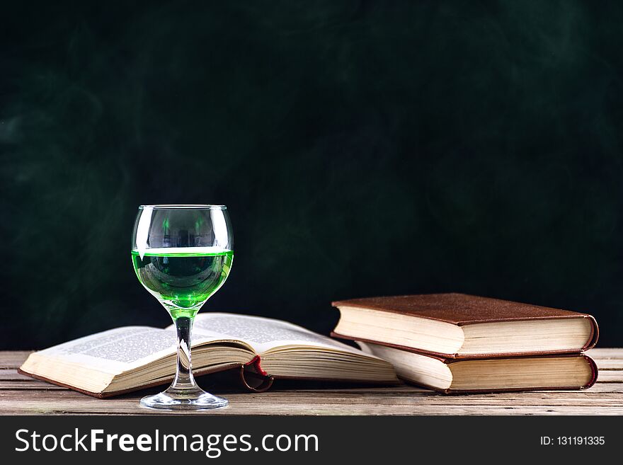 Absinthe drink in glass and books with candle in candlestick burning on retro wooden desk and smoky dark background. Green fairy inspiration and muse of writers and artists