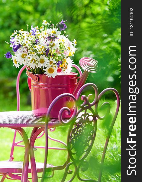 Colorful wild flower bouquet in a pink watering can on a garden chair